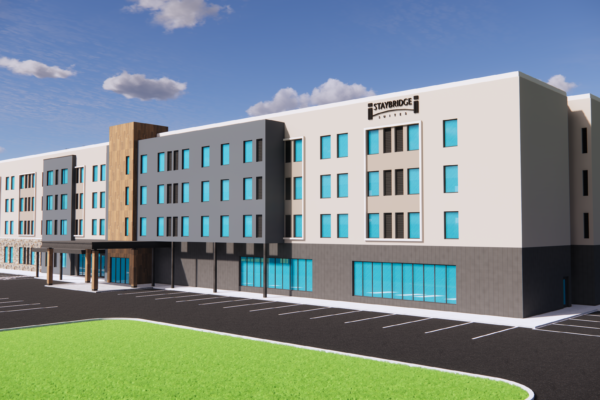 A rendering of the Staybridge Suites hotel planned for Kincardine, Ontario. The building is 4 stories high, modern exterior with wood tones and dark grey with light beige, many windows on the ground floor and exterior ground level parking.