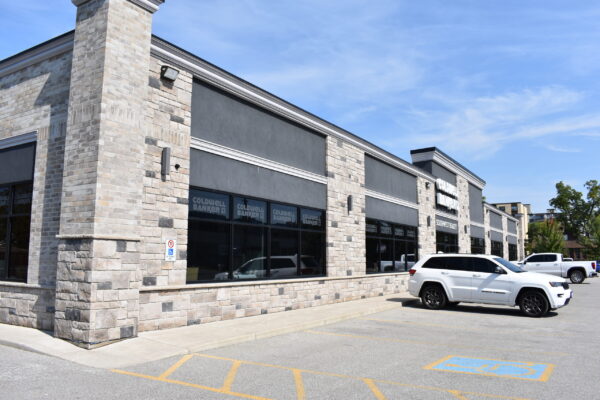 Front left view of the Coldwell Banker Southwest Realty building. One-story commercial building with stone and grey brickwork, tinted windows throughout, and on-site parking in front. The building has a white Coldwell Banker sign on the front.