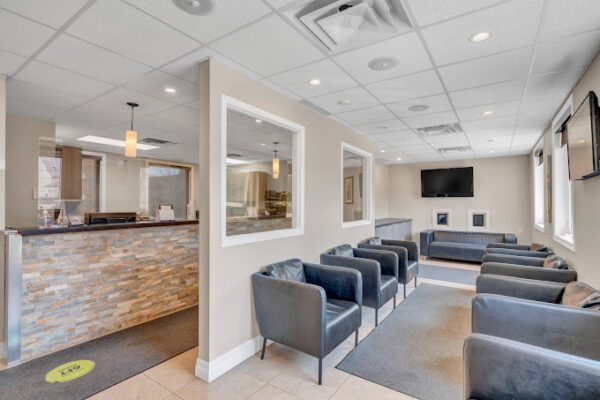 Interior view of Lambton Family Dental's reception area with stylish windowed wall partition and waiting room with cozy blue chairs, recessed lighting.