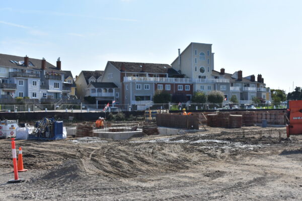 Venetian Boulevard Condominium building in the construction phase. The foreground shows heavy equipment and workers working on foundation for a new building, while another completed building stands in the background, a tall colourful condominium building.